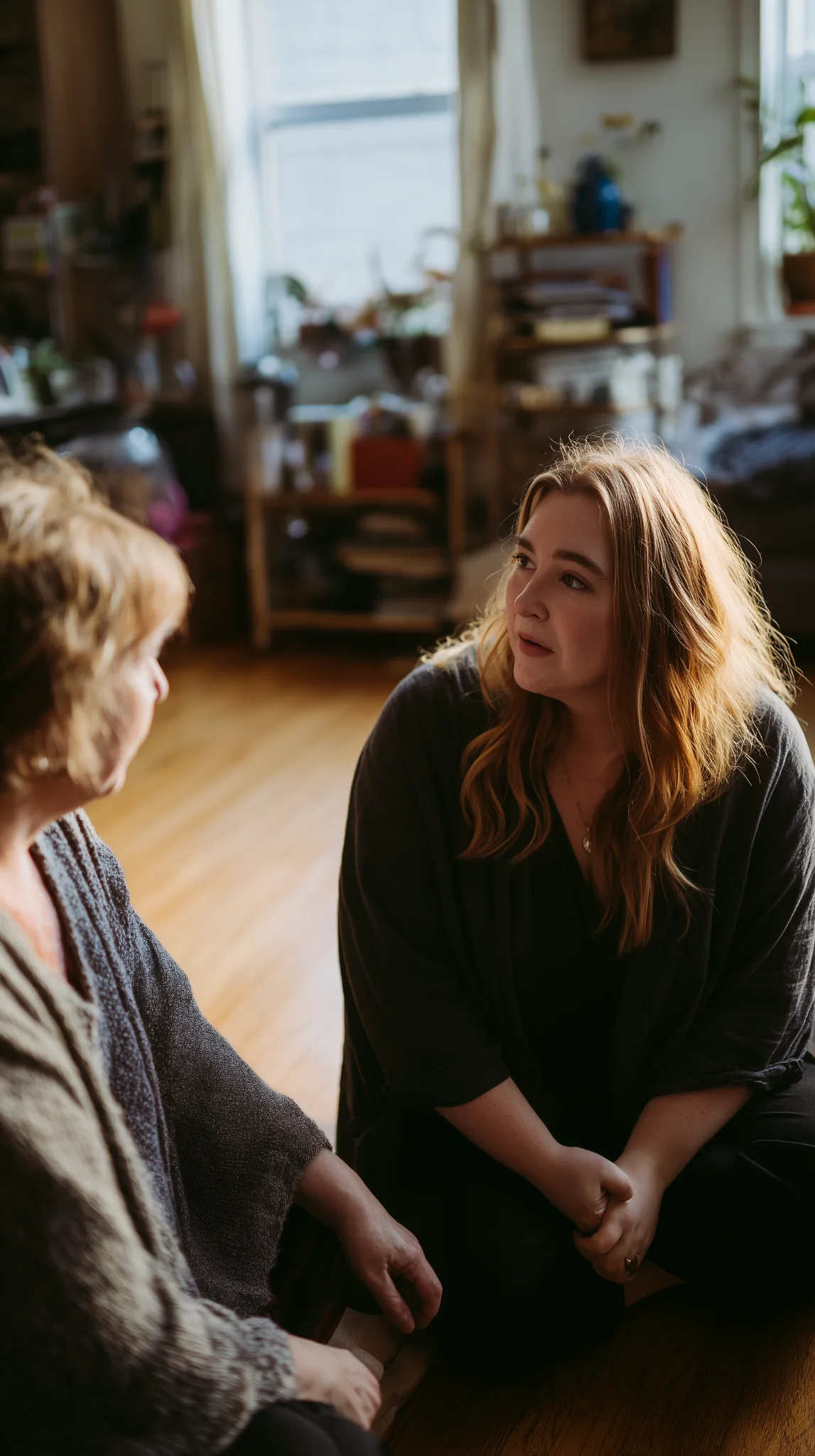 two-women-supportive-conversation-home Two women sitting together at home, engaged in a quiet, supportive conversation in a softly lit living space.