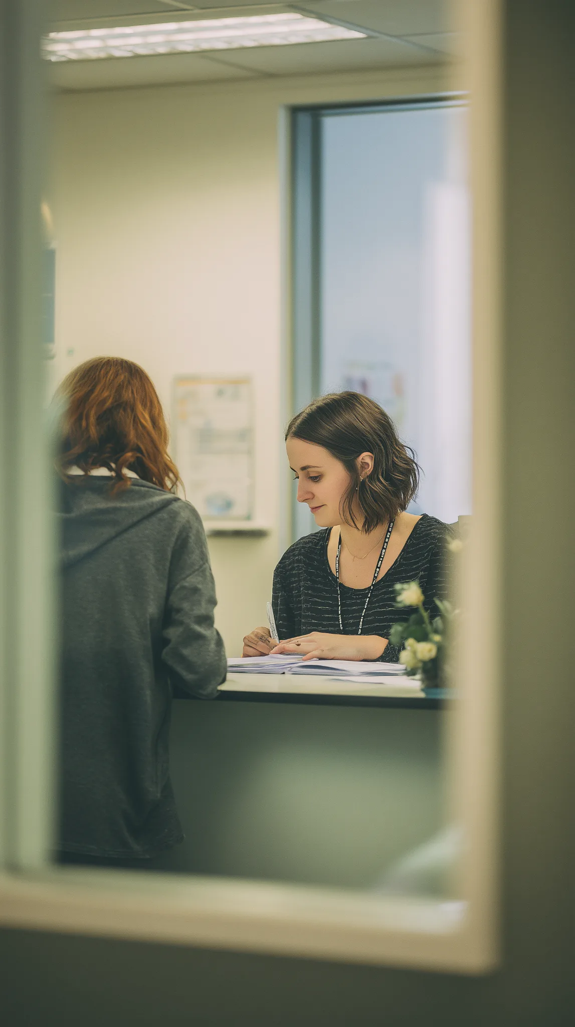 youth-check-in-support-desk-optimised Youth support worker completing paperwork at a reception desk while a young person checks in at a community support service